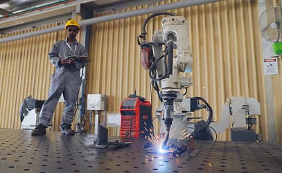 A robotic welding arm at work on a fixture table, an operator behind it