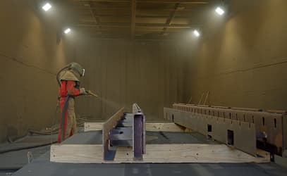A technician blasting steel sections in the enclosed blasting booth